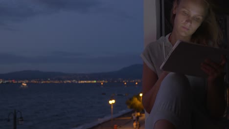 woman with pad on hotel balcony at night