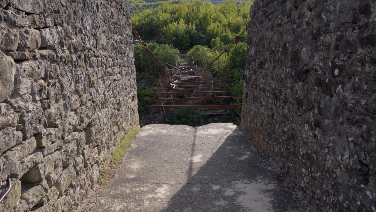Vista dalle spesse mura di una fortezza in pietra su un vecchio ponte pedonale sospeso in legno, logoro.