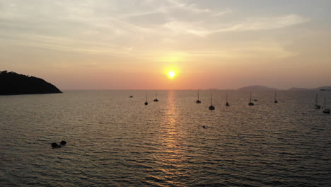 Océano-Tranquilo-Con-Una-Puesta-De-Sol-Dorada,-Barcos-Y-Montañas-Al-Fondo