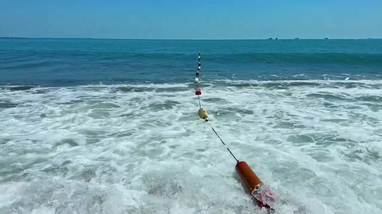 Tali pancing membentang melintasi samudra dengan pelampung sebagai penanda jalan saat ombak menghantam pantai di hari yang cerah