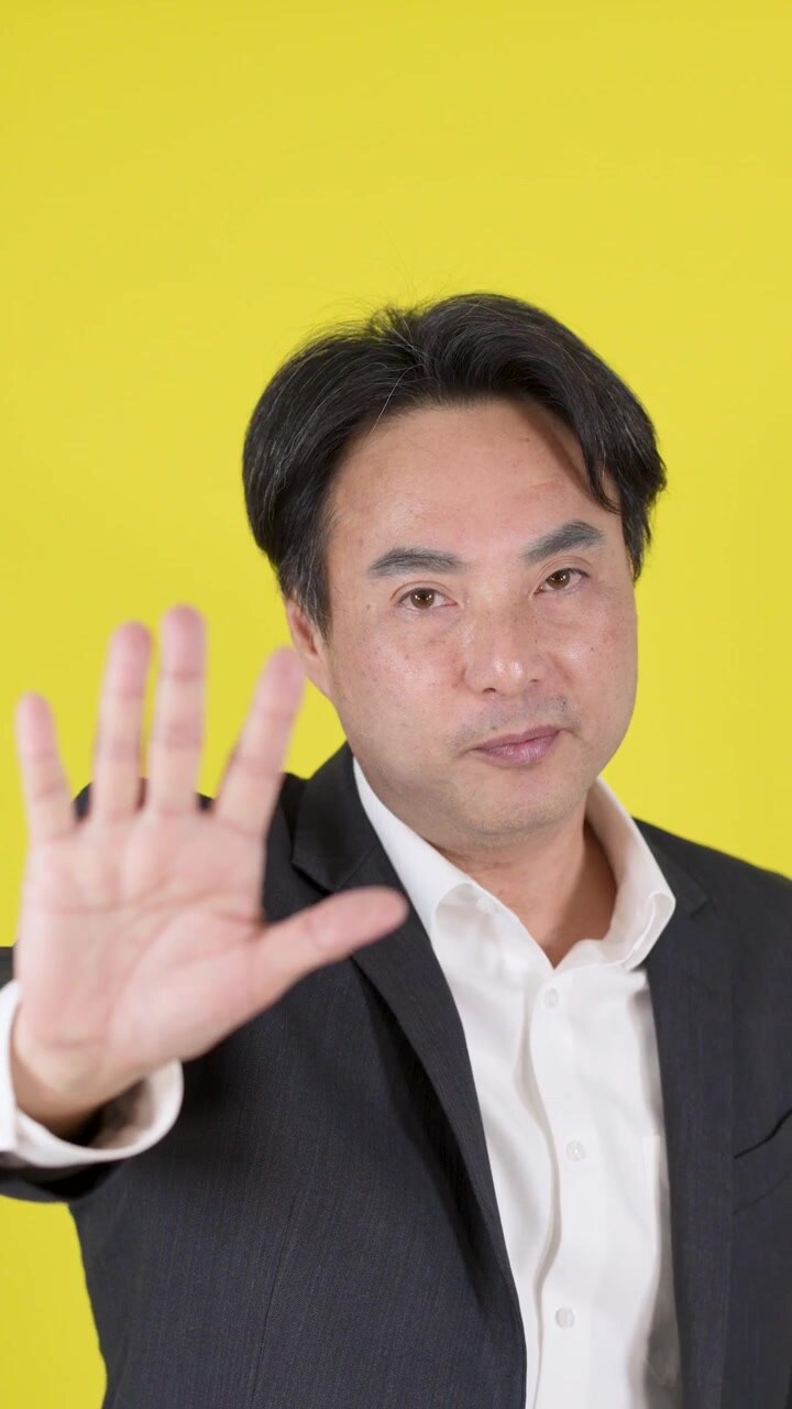 Man in suit raises hands in warning, serious face, studio lighting, yellow background, medium shot