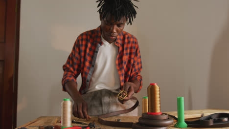 focused african american craftsman using tools to make a belt in leather workshop