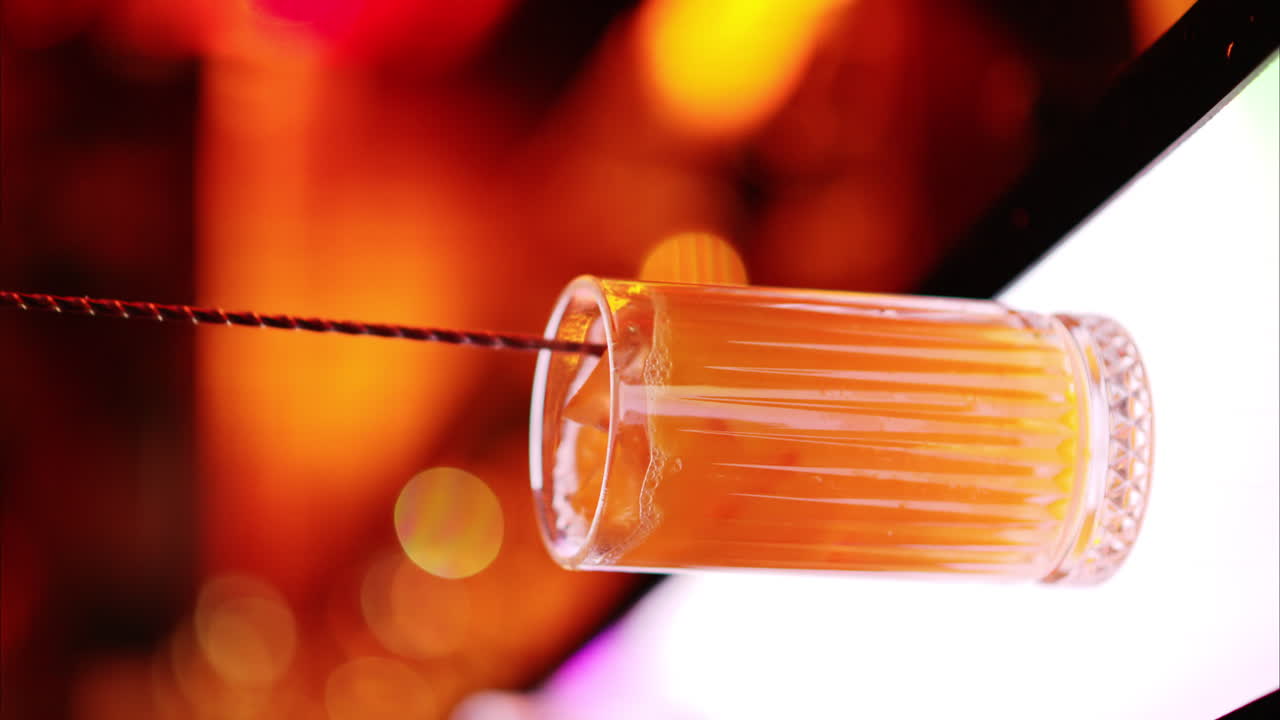 Barman che prepara e mescola un cocktail con whisky e liquore alcolico al bar di notte con luci al neon rosse, slow motion, schermo verticale