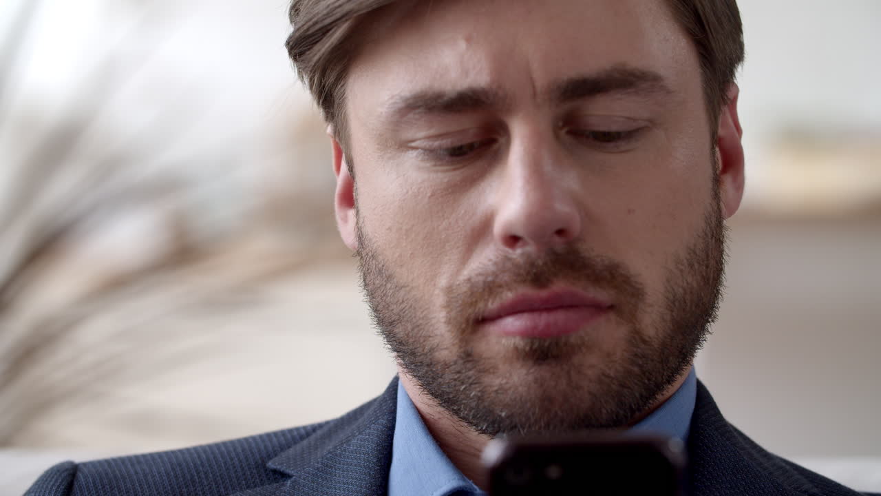 Primo piano: uomo concentrato che legge un messaggio sullo smartphone nel suo ufficio a casa.