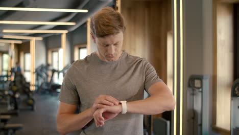 confident fitness man using smartwatch at gym. sportsman standing in sport club