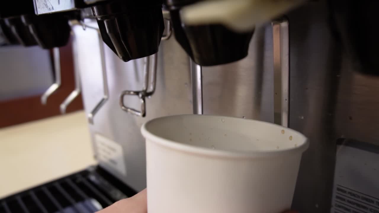 Soda dispenser machine filling a white paper cup with black, cola flavored fizzy liquid