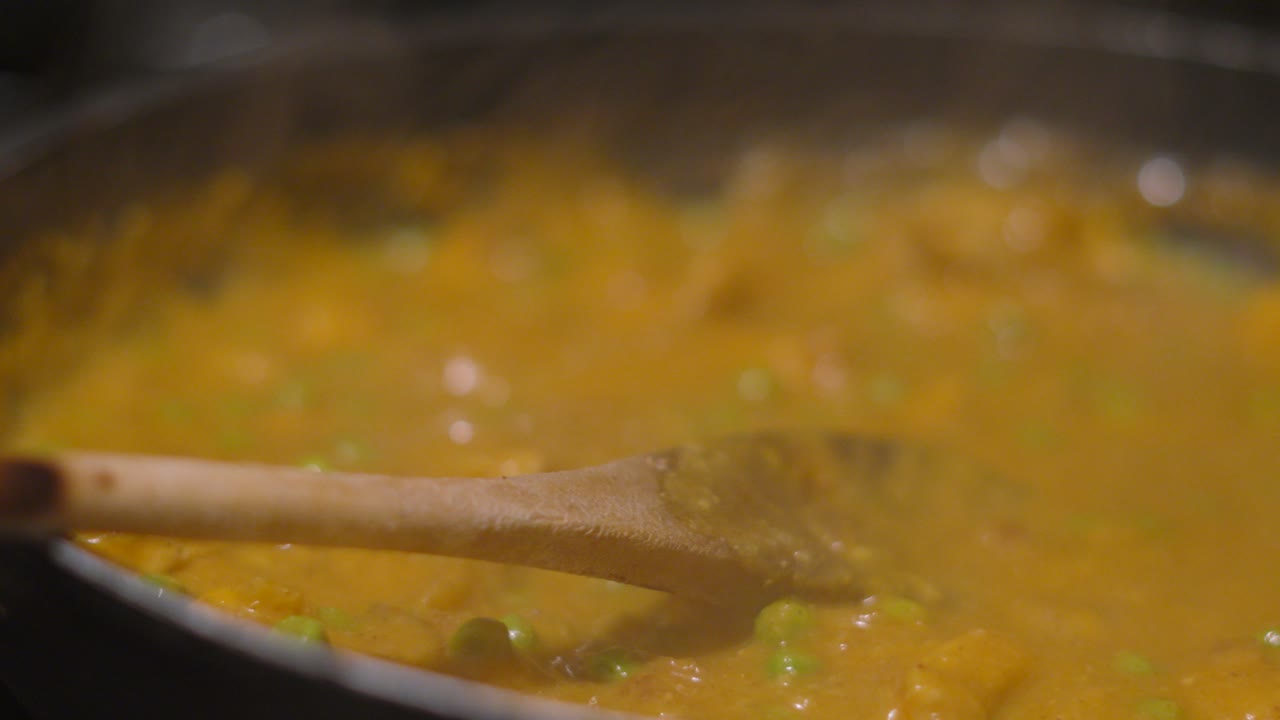 Primo piano di un ricco e dorato pollo korma che sobbolle delicatamente in una padella. Il vapore sale mentre la densa salsa a base di frutta secca ricopre succulenti pezzi di pollo.