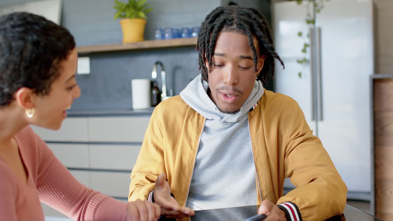 Una coppia di etnie diverse usa un tablet per condividere una presentazione e discutere i dettagli al bancone della cucina