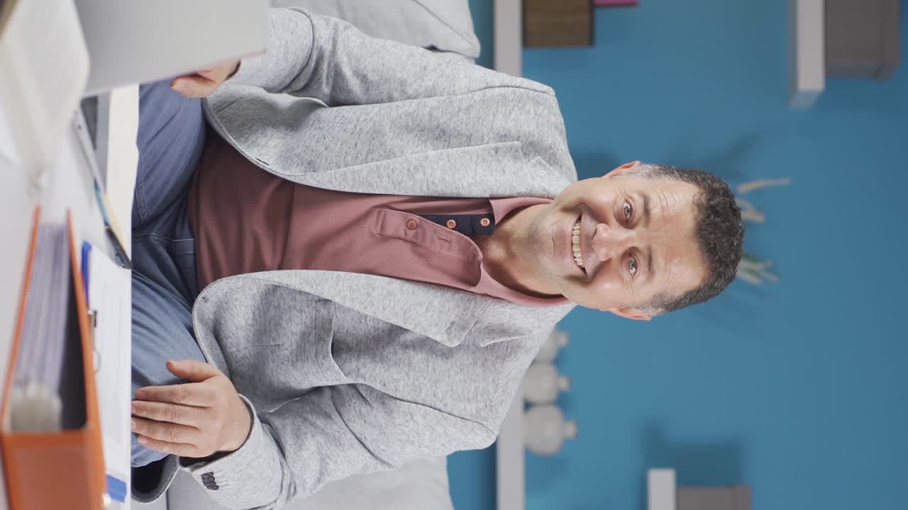 Vertical video of Home office worker old man looking at camera with excitement and feeling happy.