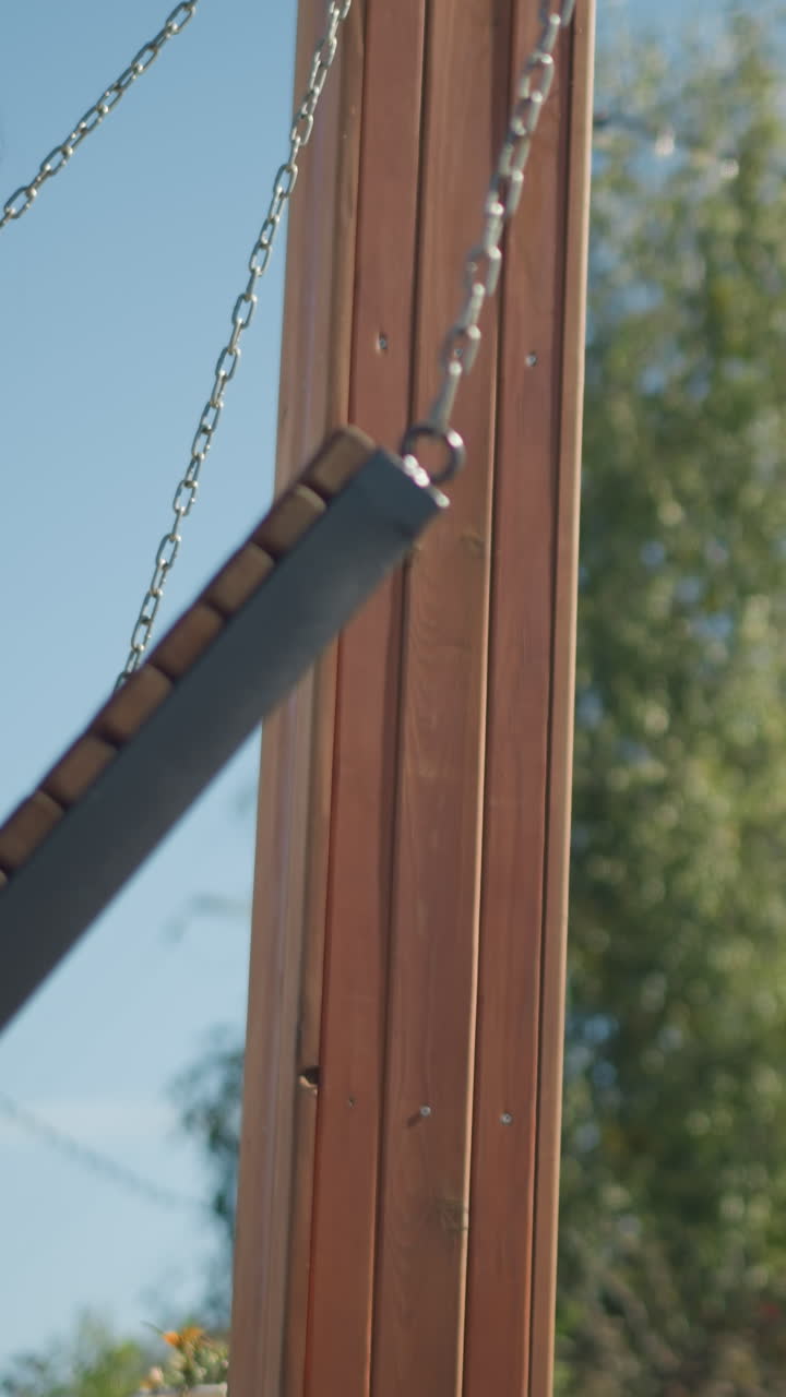 vista lateral de cerca de una mujer sentada en un columpio de madera, el cabello soplando suavemente en el viento, rodeada de exuberante vegetación en un tranquilo parque