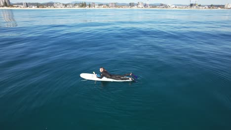 surfer lying on surfboard and floating on calm ocean - drone shot