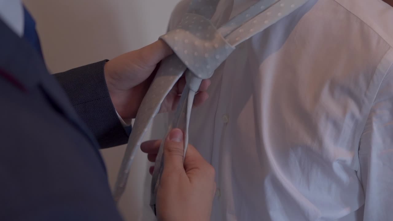 Close up of hands adjusting a light grey tie over a crisp white dress shirt