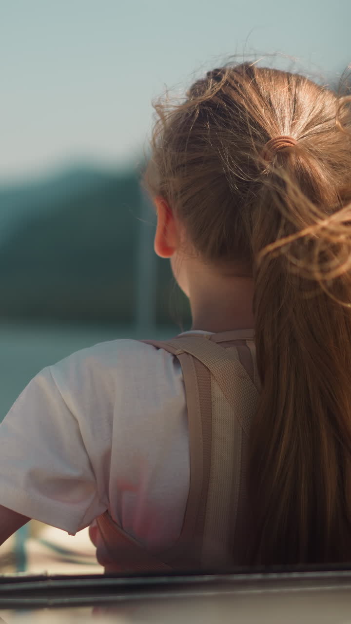 niña con corsé ortopédico mira en la distancia montando una lancha a motor en la bahía del mar vista trasera. niño con lesión en la espalda descansa en un yate en el océano en un día de verano
