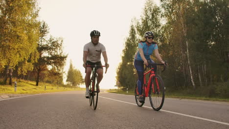 steadicam shot of two healthy mem and woman peddling fast with cycling road bicycle at sunset