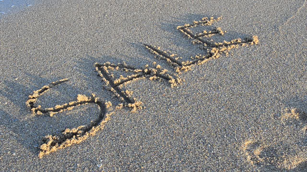The inscription sale on sand. The inscription is washed away by a sea wave. Shooting on the beach