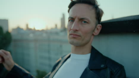 young man deep in thought, sitting on top of high building, black leather jacket, sunset, lens flare, hand held