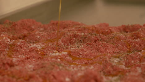 oil pouring onto raw beef mince in preparation for handmade burger production