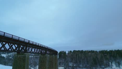 Aufsteigende-Luftaufnahmen-Von-Hohen-Steinsäulen-Und-Der-Stahlkonstruktion-Einer-Alten-Eisenbahnbrücke-über-Einem-Verschneiten-Tal