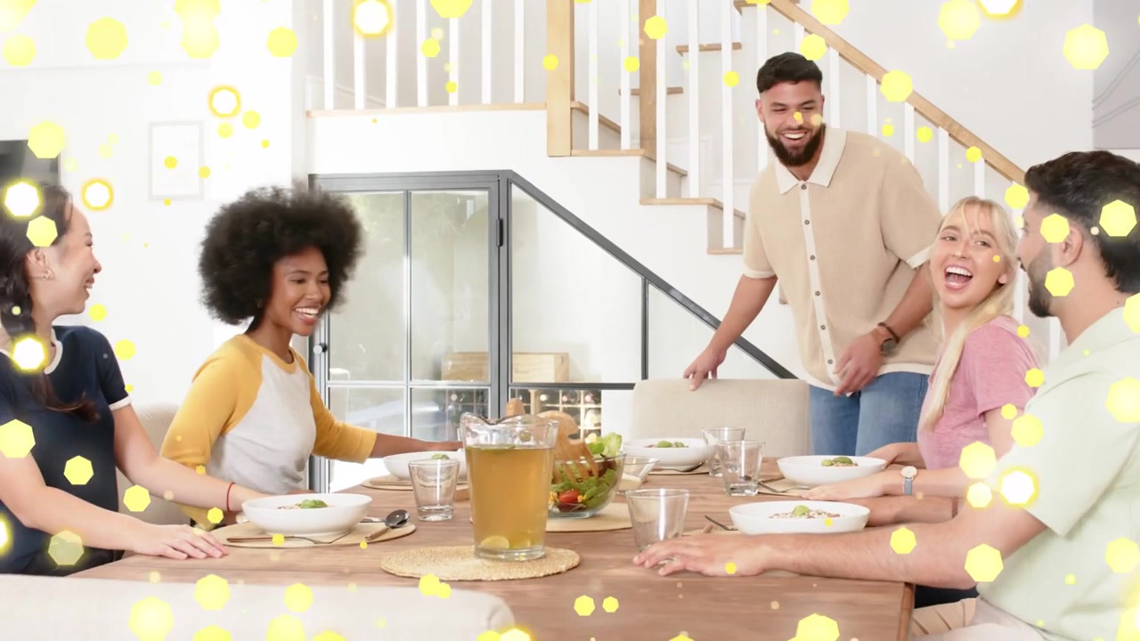 Cinq adultes réunis autour d'une table, une femme apportant une salade pour commencer un repas partagé, avec un bokeh jaune apparaissant
