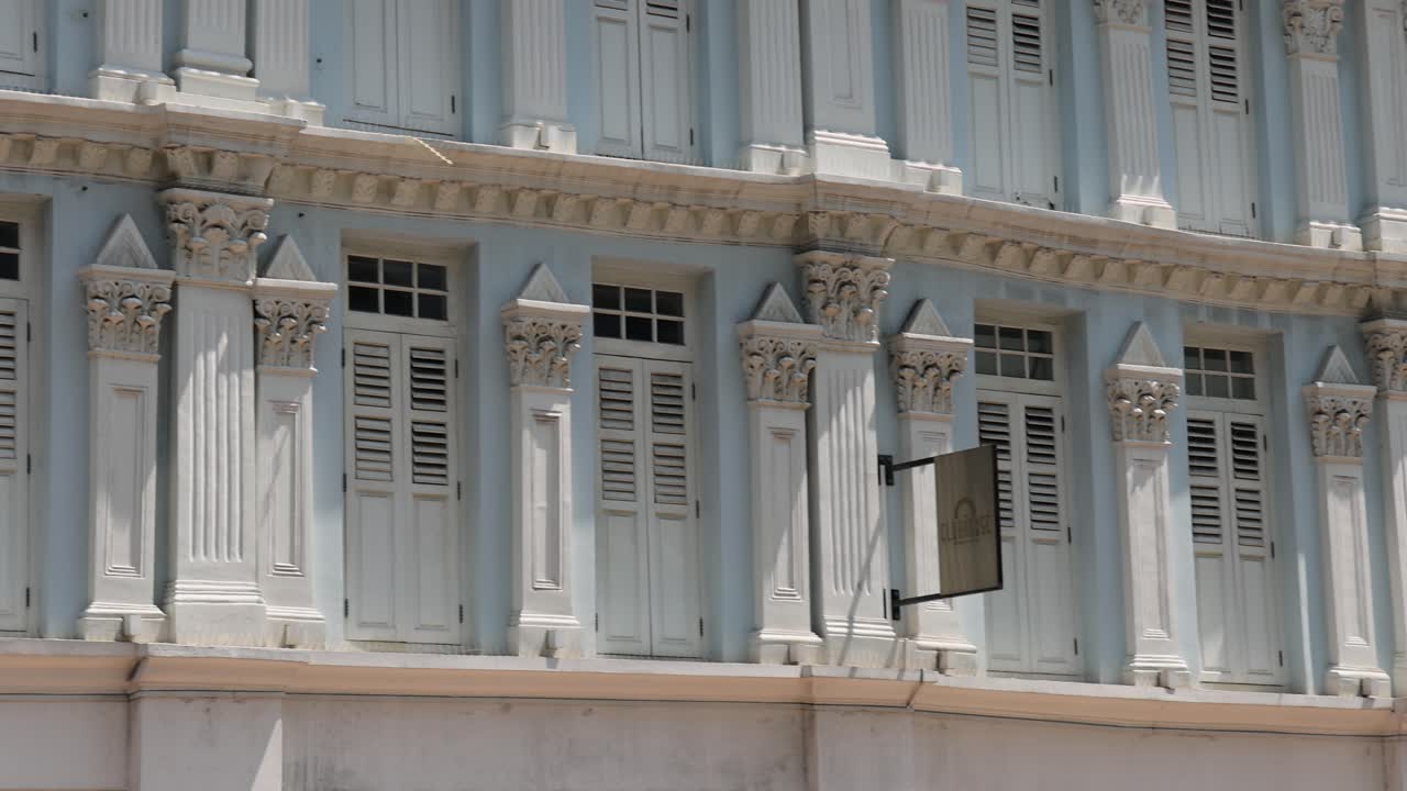 Camera pans across colorful, traditional shophouse facades on a sunny street in Singapore, highlighting architectural details and vibrant signage under bright daylight