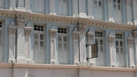 camera pans across colorful, traditional shophouse facades on a sunny street in singapore, highlighting architectural details and vibrant signage under bright daylight