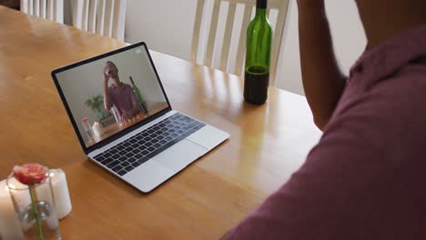 Mid-section-of-african-american-man-drinking-wine-while-having-a-video-call-on-laptop-at-home