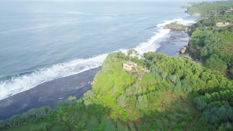 orbit drone shot of waves reaching green coastline of indonesia with private house on the top of cliff