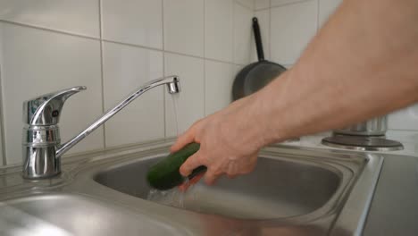 hombre lavando un calabacín con agua corriente. cocinando