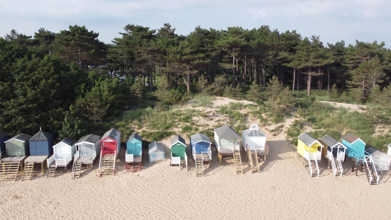 cabañas de playa en la playa de arena con bosques detrás de dolly tracking slider drone shot en wells-next-the-sea north norfolk uk