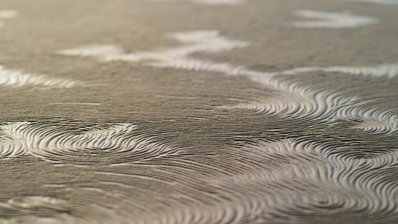 Slow natural movement reveals patterned sand ripples across flat coastal ground, with sharp shallow grooves, layered striations, damp reflective patches, and softly blended detail, with sand, ripple