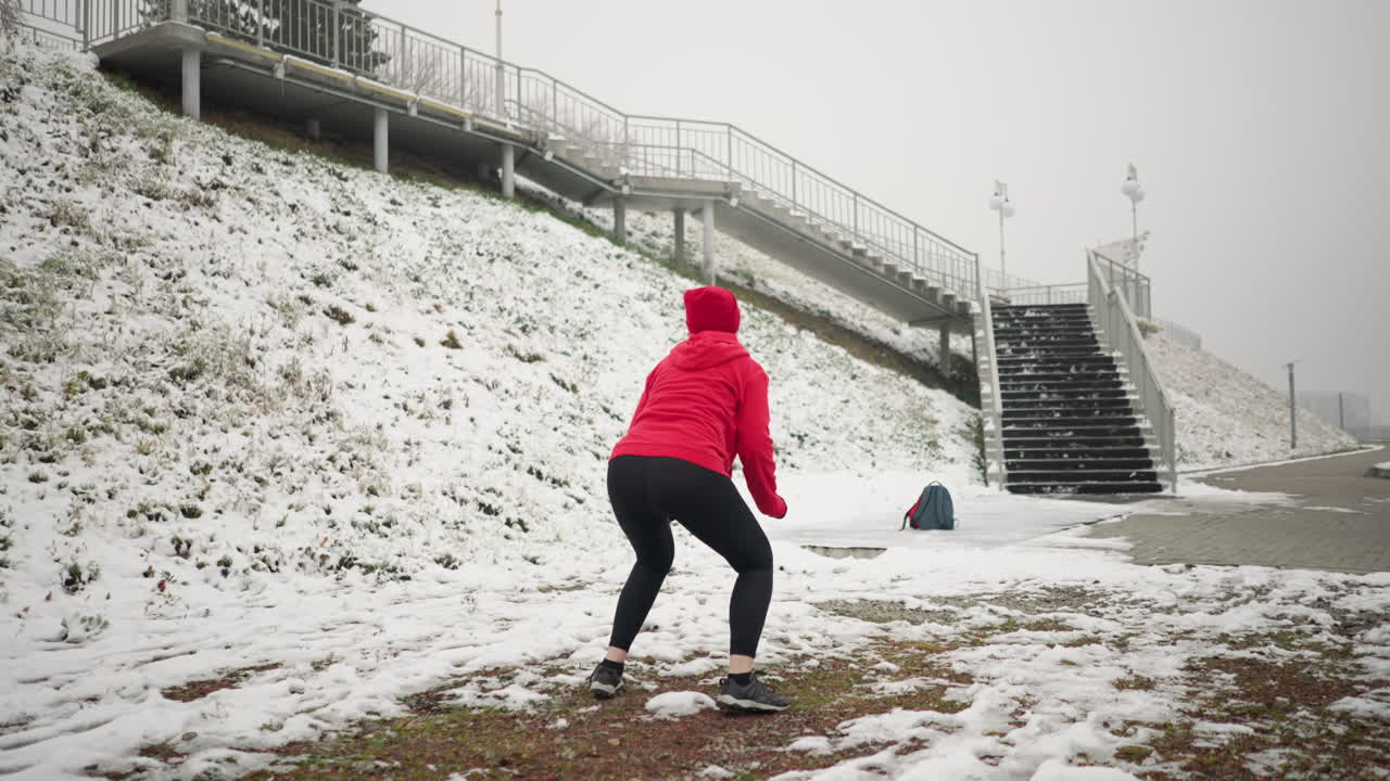 은 후디와 검은 장갑을 입고 눈 인 땅에서 겨울 야외 운동 중에 점프 스을 수행하는 여성의 뒷면, 무대에는 철 철로와 함께 눈 은 언덕, 안개 분위기가 포함됩니다.