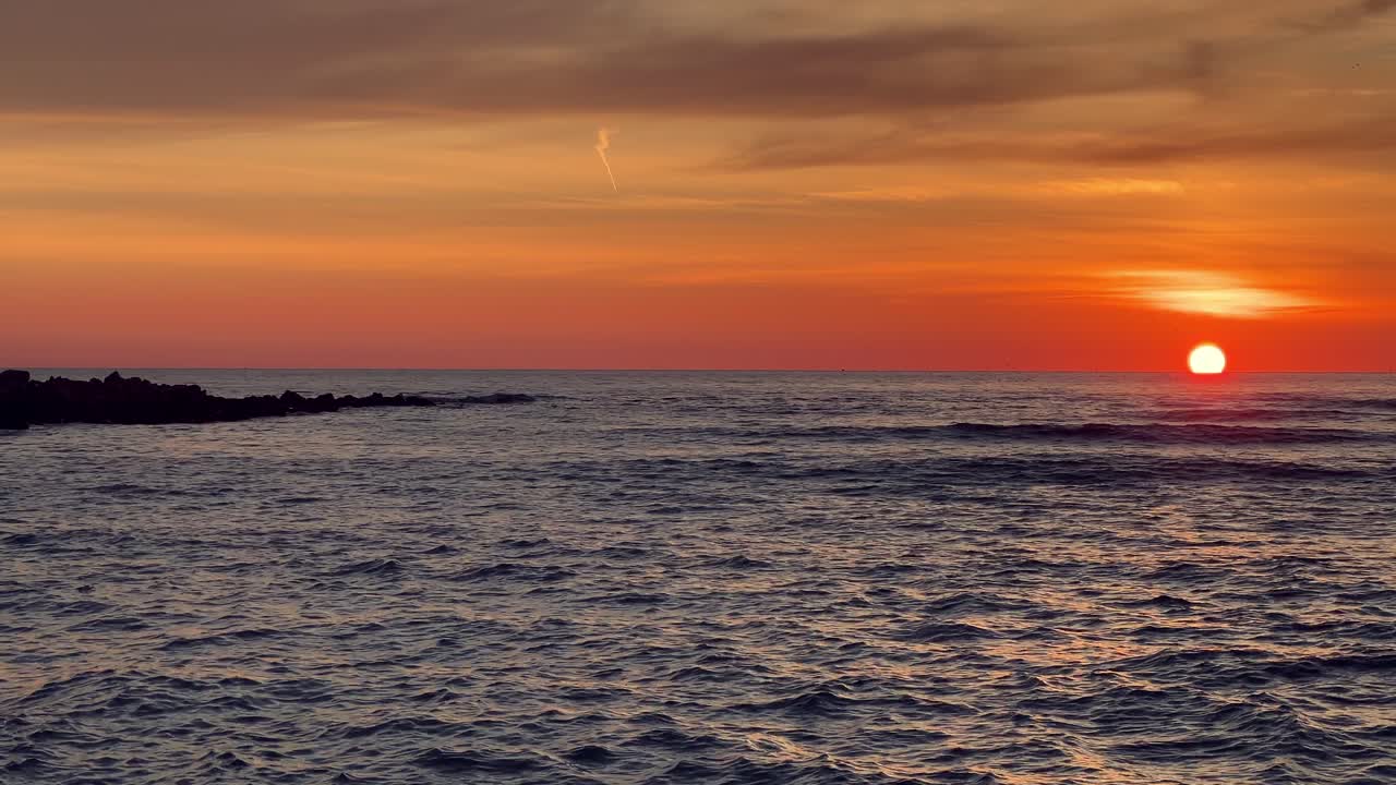 la luz del sol de la hora dorada pinta el cielo con tonos cálidos mientras el sol se sumerge debajo del horizonte, proyectando un resplandor hipnotizante sobre las suaves olas del océano y una costa escarpada.