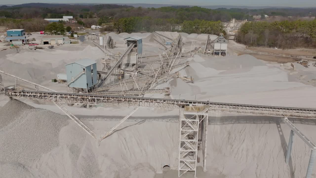 Aerial footage rotating around a group of conveyor belts moving rock in a quarry.