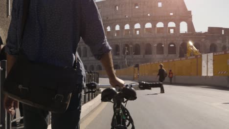 young hipster man walking with bike in rome colosseum on sunny day slow motion camera car steadycam