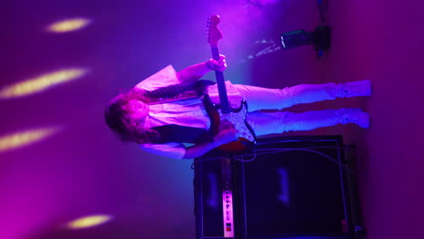 vertical video of an energetic male rock band guitarist playing in neon light and smoke. dancing guitar player in the studio and bright colors