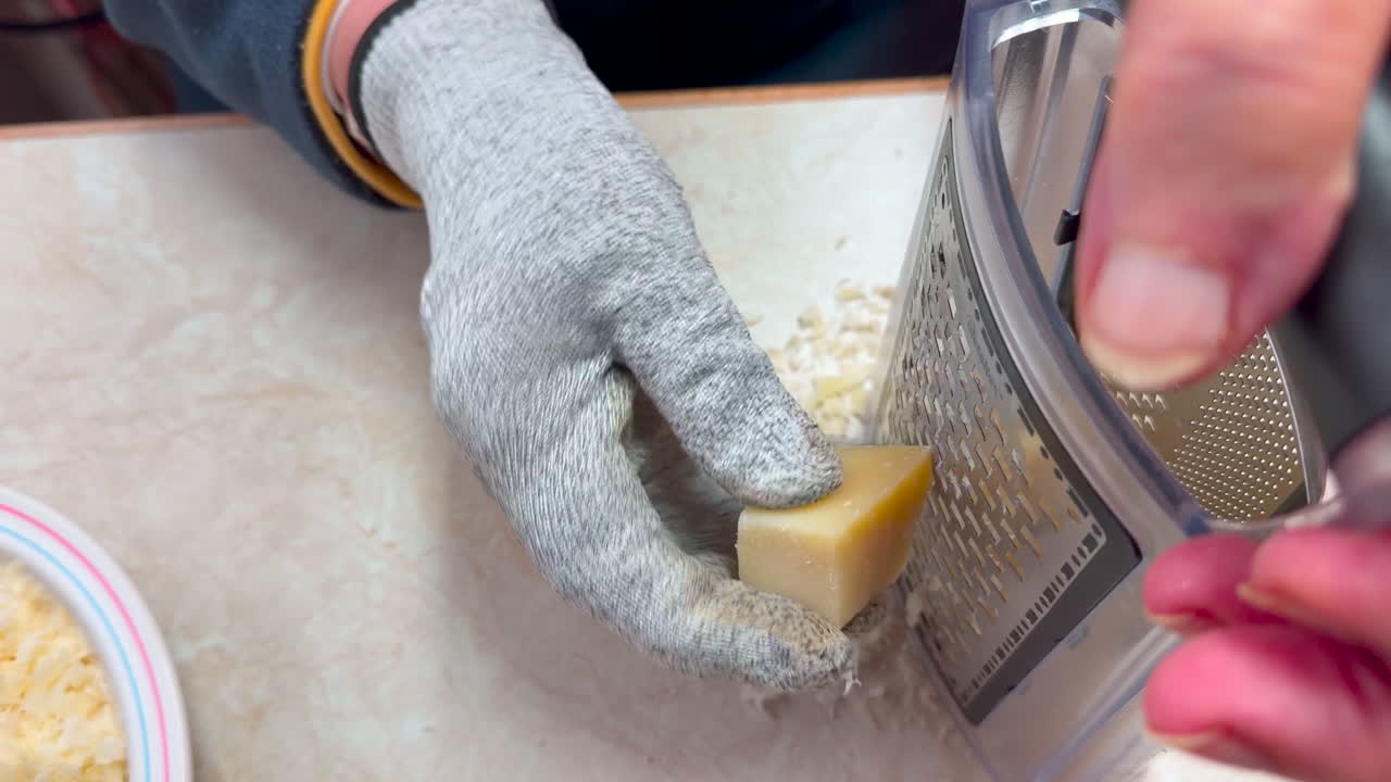 Una casalinga grattugia il formaggio usando una grattugia, indossa un guanto protettivo sulla mano destra, push-in shot
