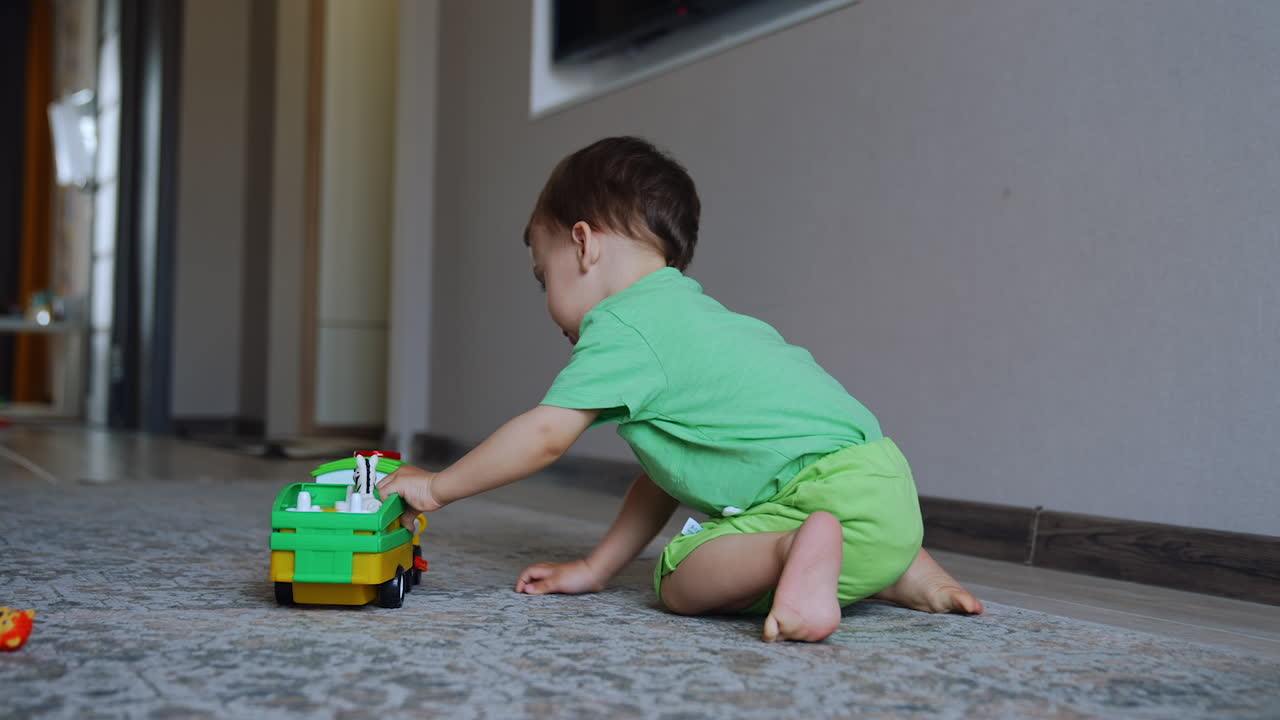 Rear view of a child playing on the floor. Kid in green clothes is busy with his toy train.