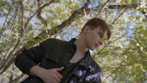 young soldier preparing for next stage of journey in the lonely forest, pulling off jacket and genuflecting, and picks up headband from black bag in readiness for the outdoor forest adventure