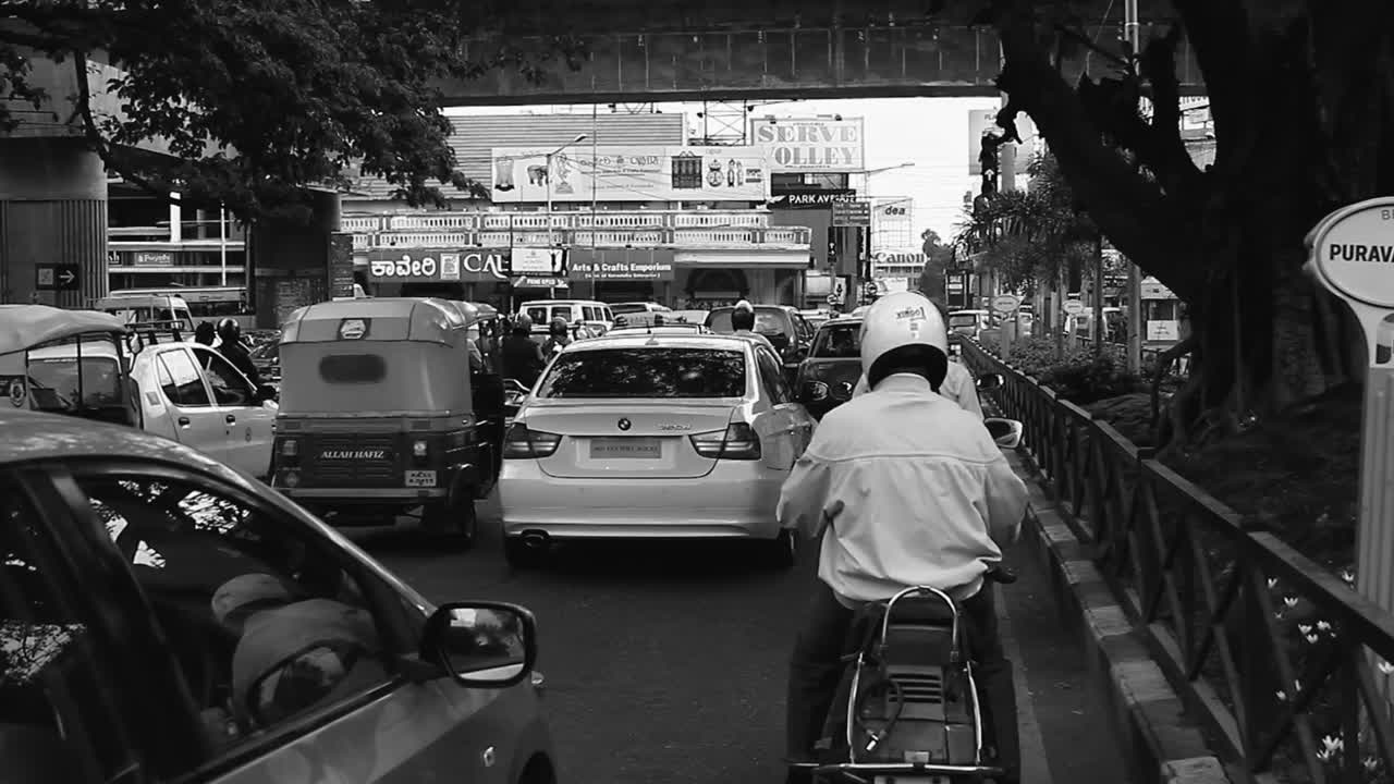 Heavy traffic with cars and motorbikes fills a busy street under an overpass in Bangalore, black and white