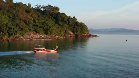 Cinematic-aerial-tracking-shot-capturing-a-traditional-gondola-fishing-boat,-sailing-out-to-the-ocean-to-catch-fish-at-beautiful-sunset-golden-hour,-Langkawi-island,-Malaysia,-Southeast-Asia