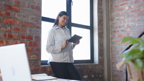 smiling woman holding tablet while standing by window in modern office