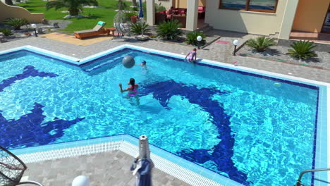 panoramic drone shot circling a family playing with ball in a pool, sunny day