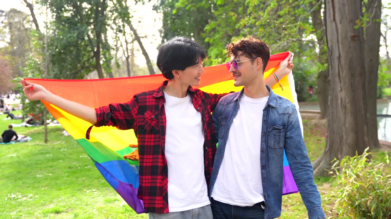 Gay couple celebrating pride in the park with rainbow flag