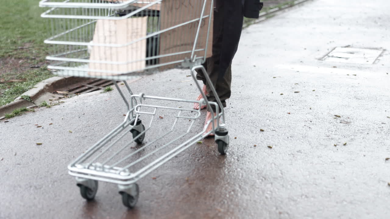 persona sin hogar caminando en la lluvia con un carrito de compras