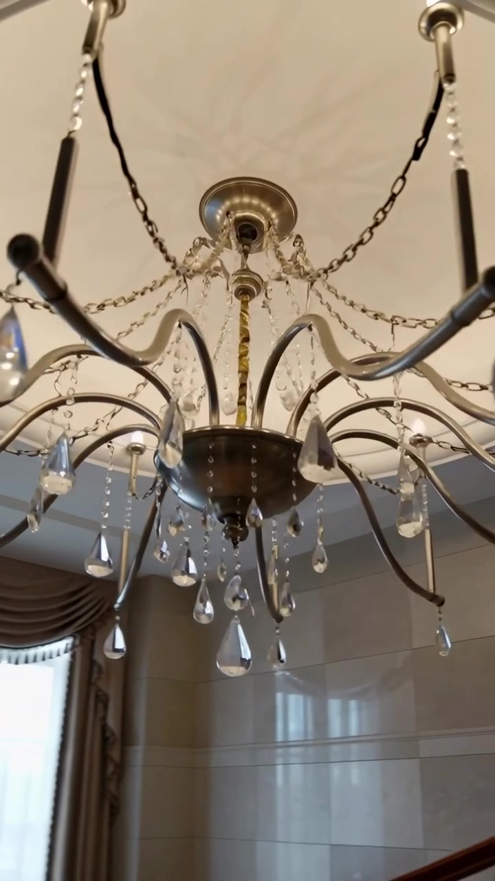 Vertical video: Pulling back camera revealing chandelier shining crystals in foyer, stairs