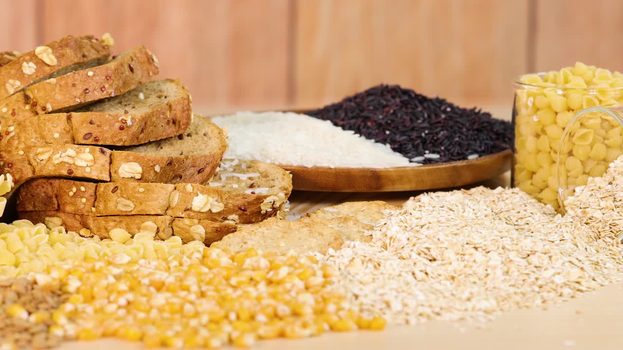 A variety of grains, pasta, and bread arranged on a wooden table with natural lighting