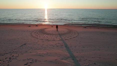 Luftaufnahme-Eines-Kunstsandstrandes-An-Der-Kurischen-Nehrung-Mit-Der-Silhouette-Einer-Person,-Die-In-Der-Mitte-Steht,-Mit-Sonnenuntergang-Im-Hintergrund