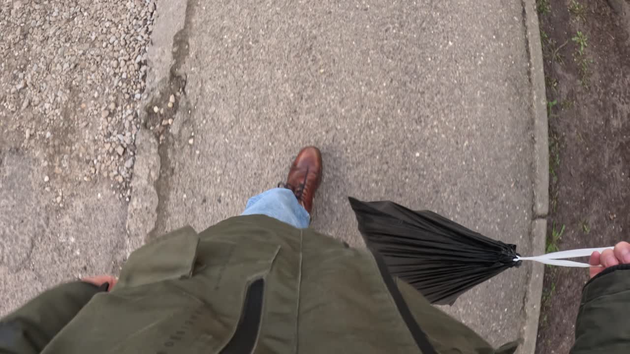 Top down view of a man walking on the street and taking out trash. POV of garbage bag in the hands.