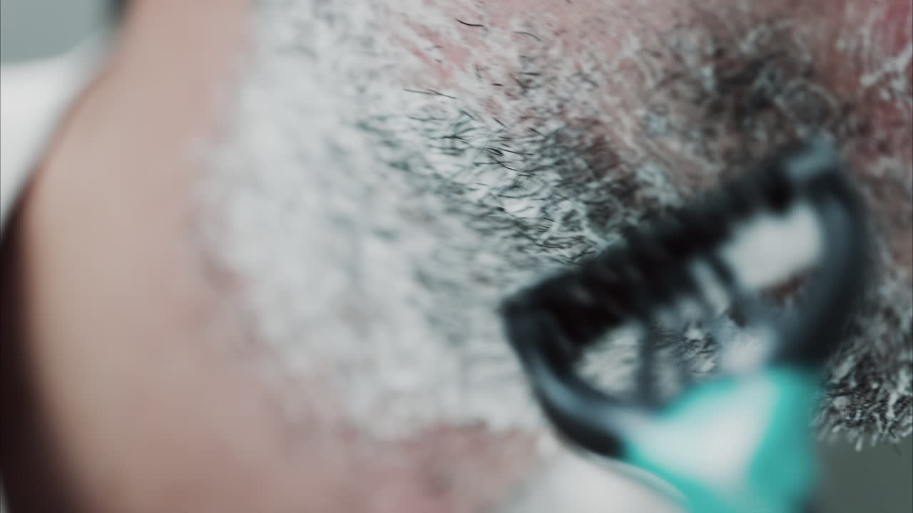 Close up of a man shaving his beard with a razor