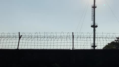 Industrial-area,-wired-fence-wall,-gas-flare-on-background,-handheld-pan